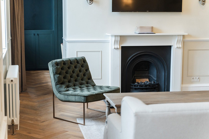A green cushioned chair in a room with wooden flooring and white walls