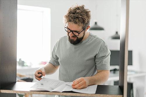 Man with beard and glasses reading a technical manual inside living room