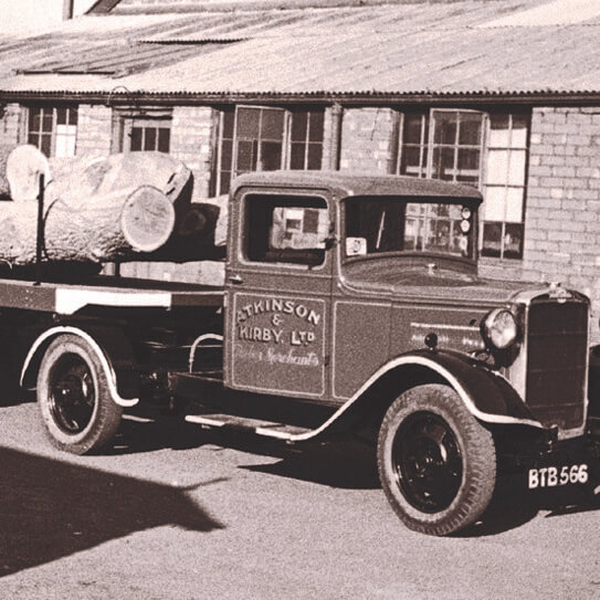 A vintage photograph of a van carrying logs outside a factory.